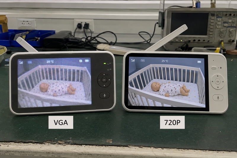 Two baby monitors side by side on a test bench &mdash; VGA unit on left, 720P unit on right, same baby doll visible on both screens