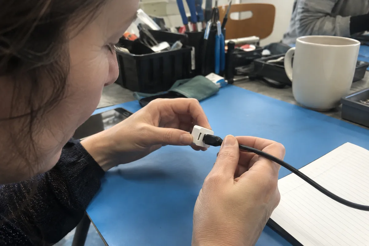 A reviewer checking a low-voltage plug connection on a blue repair mat.